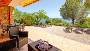 Une terrasse extérieure avec des meubles en osier, un mur en pierre et une vue sur la mer.