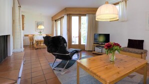 A cozy living room with a wooden table, a black chair, a sofa, a TV, and a fireplace. - Chesa Maurus A1 by Interhome (St. Moritz)