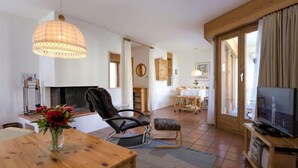A cozy living room with a wooden dining table, a comfortable chair, a TV, and a fireplace. - Chesa Maurus A1 by Interhome (St. Moritz)