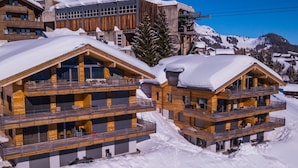 Ein schneebedecktes Chalet mit mehreren Balkonen und einer Seilbahn im Hintergrund.