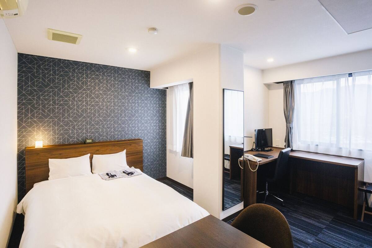 A hotel room with a bed, desk, chair, and a large mirror.