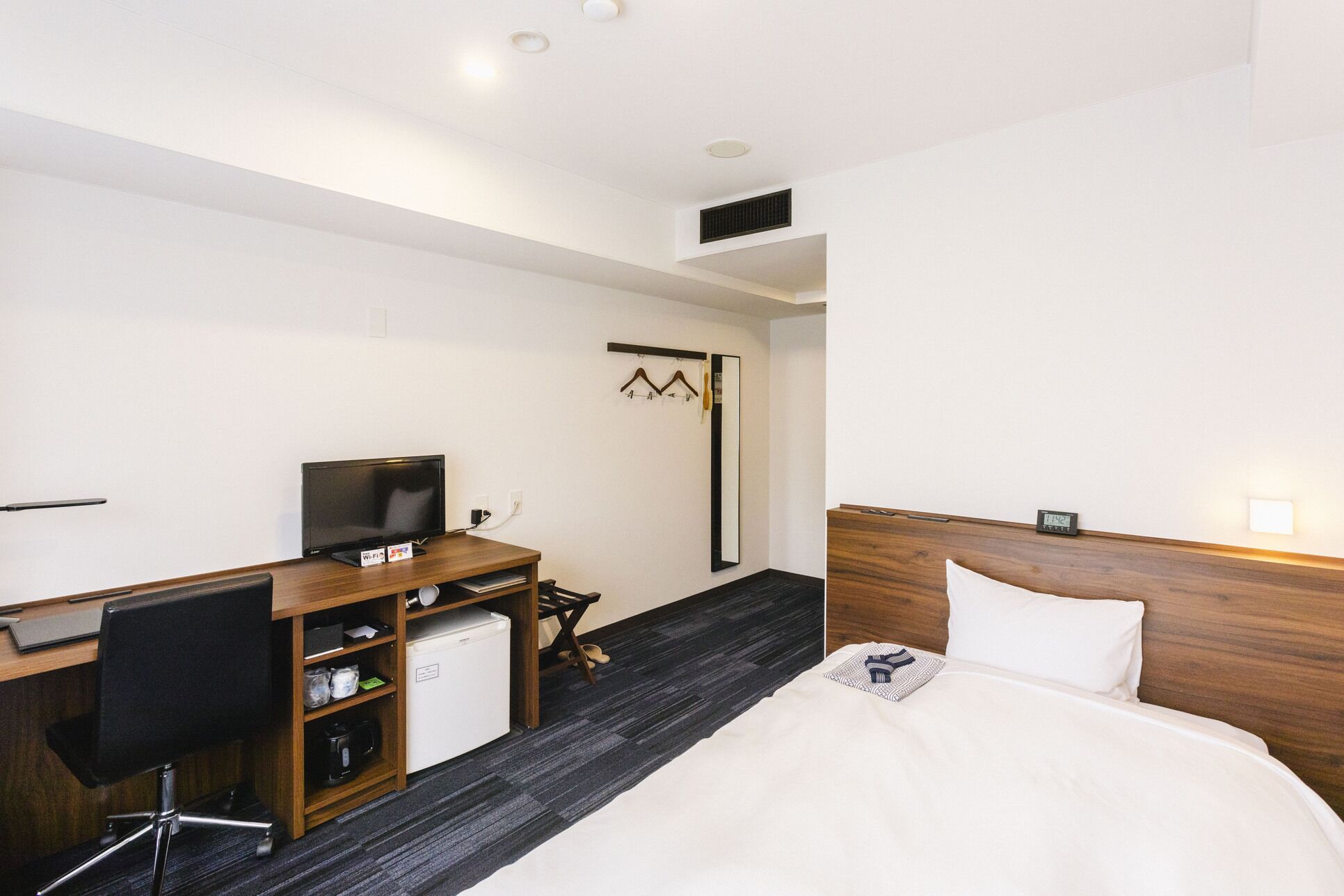 A hotel room with a bed, desk, chair, TV, and a small refrigerator.