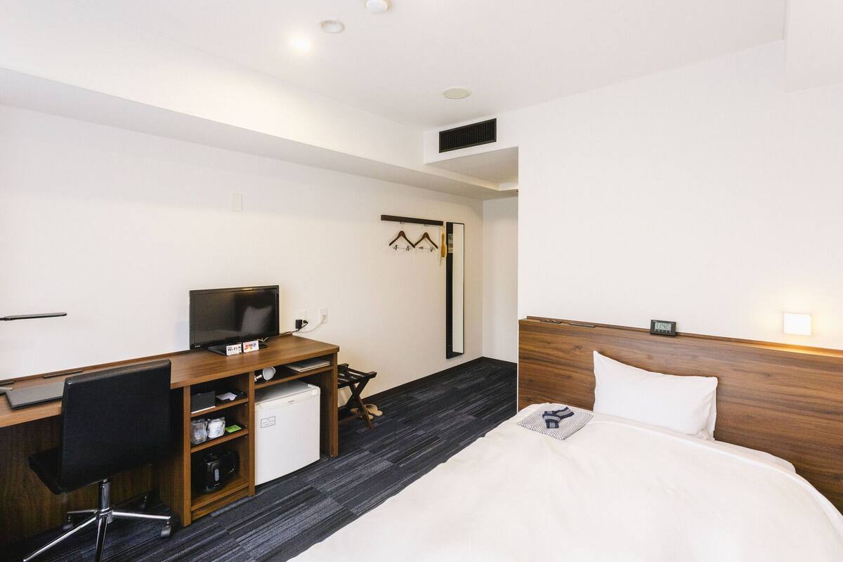 A hotel room with a bed, desk, chair, TV, and a small refrigerator.