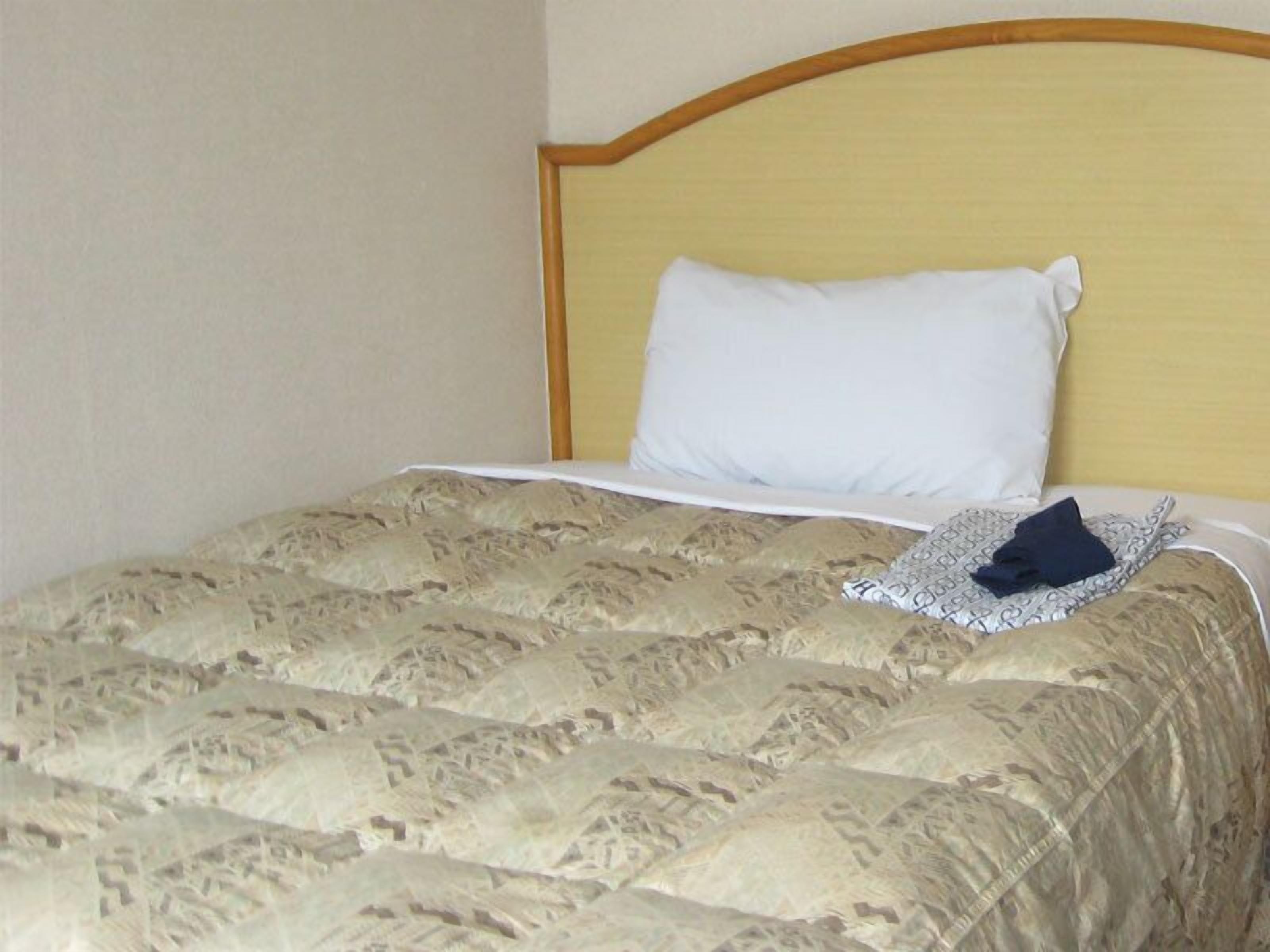 A bed with a patterned bedspread, a white pillow, and a folded dark garment on the bed.