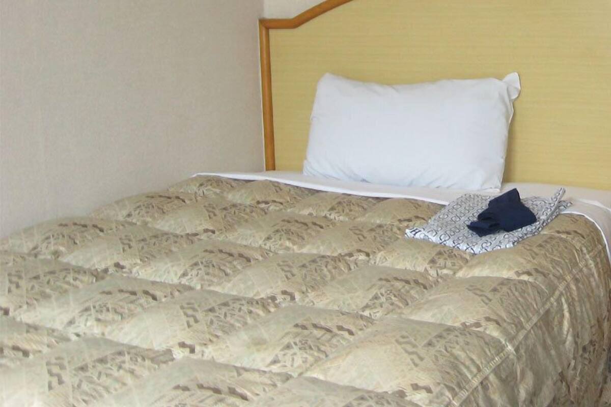 A bed with a patterned bedspread, a white pillow, and a folded dark garment on the bed.