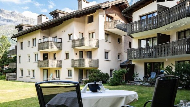 Un edificio a più piani con balconi, un prato e un tavolo con sedie allestito per mangiare all'aperto.