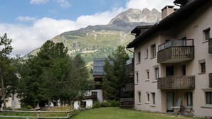 Un edificio residenziale con un balcone, un prato e montagne sullo sfondo.