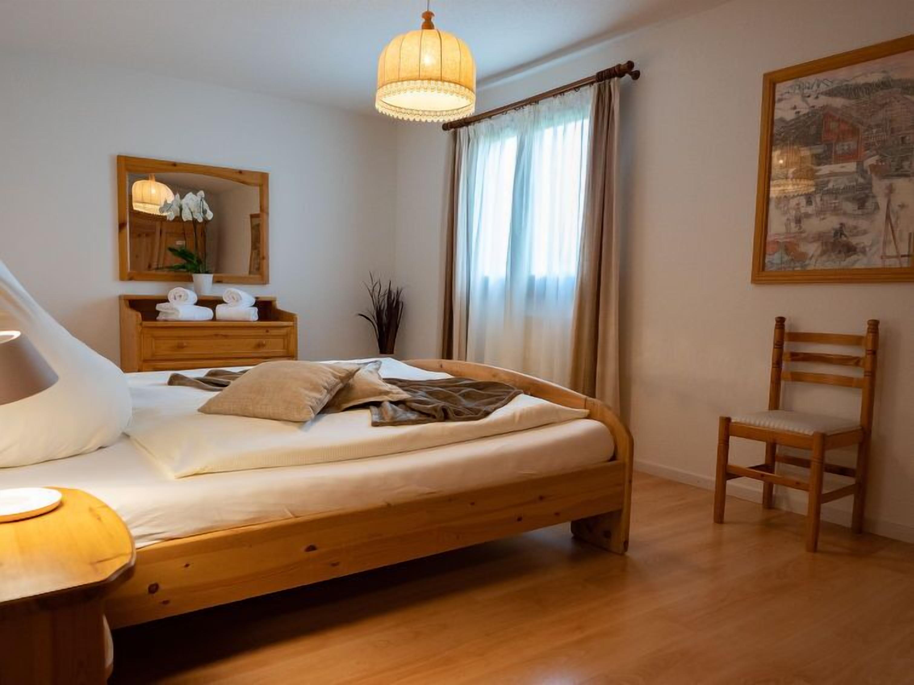 Une chambre à coucher avec un lit en bois, une table de chevet, une chaise, un miroir et un tableau accroché au mur.