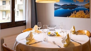 Tavola da pranzo imbandita con tovaglia bianca, bicchieri e posate, illuminata da una lampada pendente gialla.