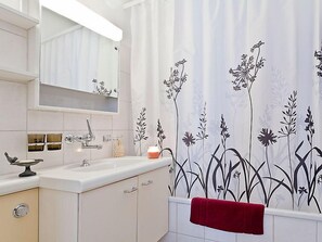 Une salle de bain avec un lavabo blanc, un miroir et un rideau de douche orné de motifs floraux.