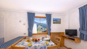 A dining area with a table set for two, a television, and a window with a view of hills. - Ginevra, Livigno, Italy (Livigno)