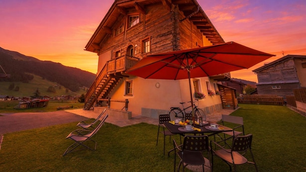 A wooden house with a balcony, a table with chairs, and a red umbrella. - Ginevra, Livigno, Italy (Livigno)