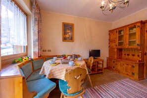 A dining area with a table set for two, a television, and wooden cabinets.