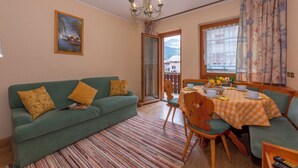 A living room with a sofa, a dining table with chairs, a chandelier, and a painting on the wall. - Paradiso Ski in - Ski  out 50m, Livigno, Italy (Livigno)