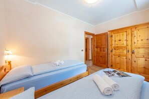 A hotel room with two beds, wooden wardrobes, and a nightstand with a lamp.