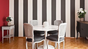 Ein Essbereich mit einem runden Tisch, sechs Stühlen, einer weißen Tischdecke und einer gestreiften Wand.