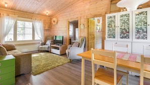 Ein gemütliches Blockhaus-Interieur mit Holzbalkendecke, Fernseher, Esstisch und einer grünen Kommode.
