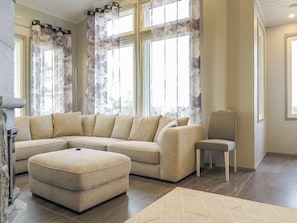 A living room with a sectional sofa, a small ottoman, and a chair. There are large windows with curtains. - Karhu b by Interhome (Inari)