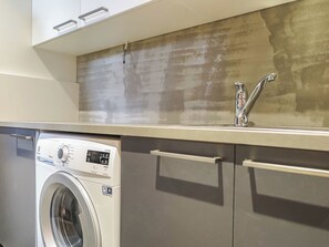 A modern kitchen with a built-in washing machine, stainless steel cabinets, and a concrete backsplash. - Karhu b by Interhome (Inari)
