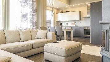 Un salon moderne avec un canapé d’angle, un petit pouf et un coin repas avec des chaises.
