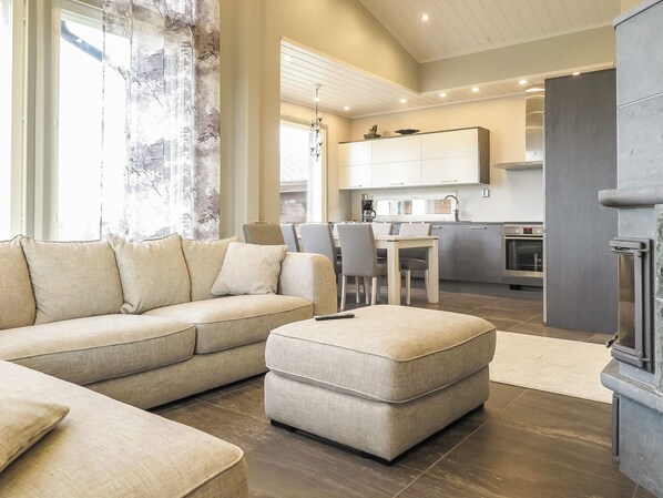A modern living room with a sectional sofa, a small ottoman, and a dining area with chairs.