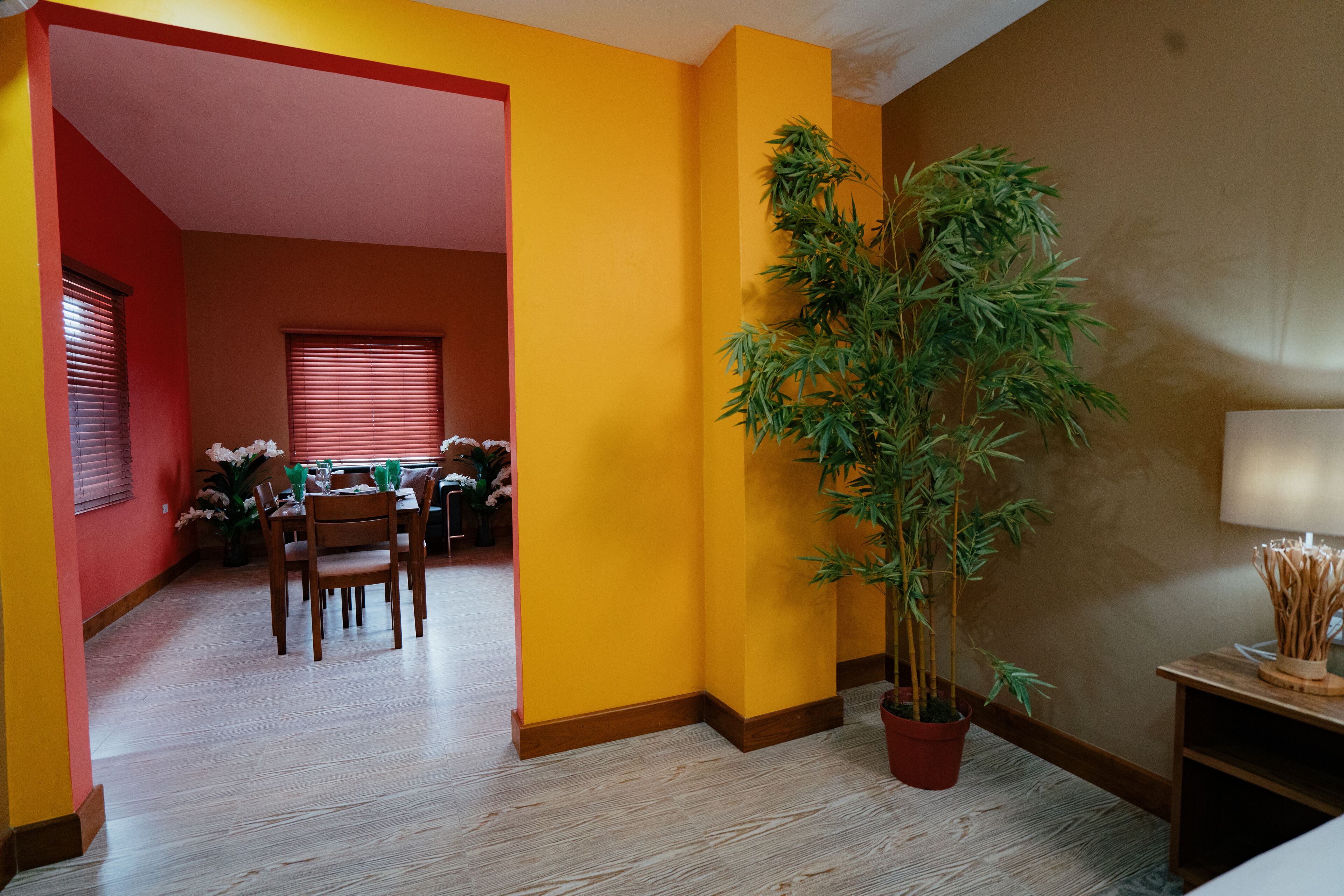 A dining area with a table set for four, a potted plant, and a lamp on a side table.