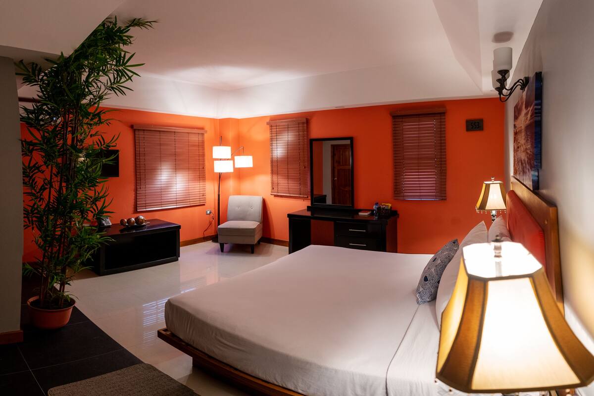 A modern bedroom with a large bed, a desk, a chair, and a potted plant.