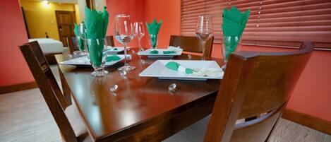 A dining table set for four with green napkins, clear glasses, and white plates.