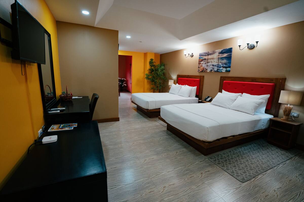 A hotel room with two beds, a desk, a TV, and a plant.