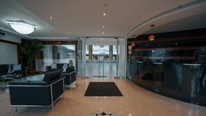 Un hall d’hôtel moderne comprenant un comptoir d’accueil, un espace salon et une vue sur la façade de l’hôtel.
