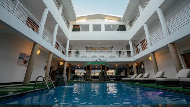 Une piscine intérieure à plusieurs niveaux, dotée d’un élément aquatique central, et entourée d’espaces de détente et d’un bar.