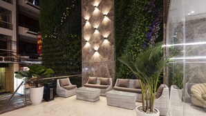 A lobby with a modern design, featuring a seating area with sofas and armchairs, a large potted plant, and a decorative wall with lights. - Nalicas Hotel (Nha Trang)