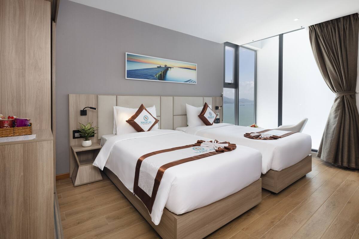 Un hotel moderno con dos camas, un ventanal grande, un cuadro de un muelle y vista al mar.