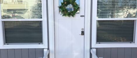 A white front door with a wreath, a number '205' above it, and a doormat with 'hello' on it.