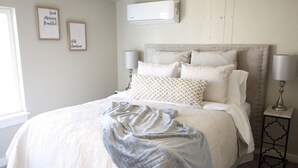 A bedroom with a large bed, two bedside lamps, a wall-mounted air conditioner, and two framed inspirational quotes. - King Cottage in Downtown Meridian (Meridian)