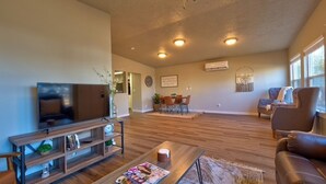 A spacious living room with a wooden floor, a ceiling fan, a flat-screen TV, a coffee table, and a fireplace. - King Cottage in Downtown Meridian (Meridian)