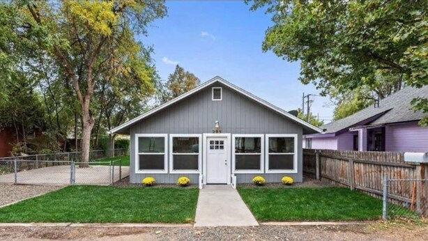 A single-story house with a grey exterior, a front porch, and a small front yard with grass and two yellow flower beds. - King Cottage in Downtown Meridian (Meridian)