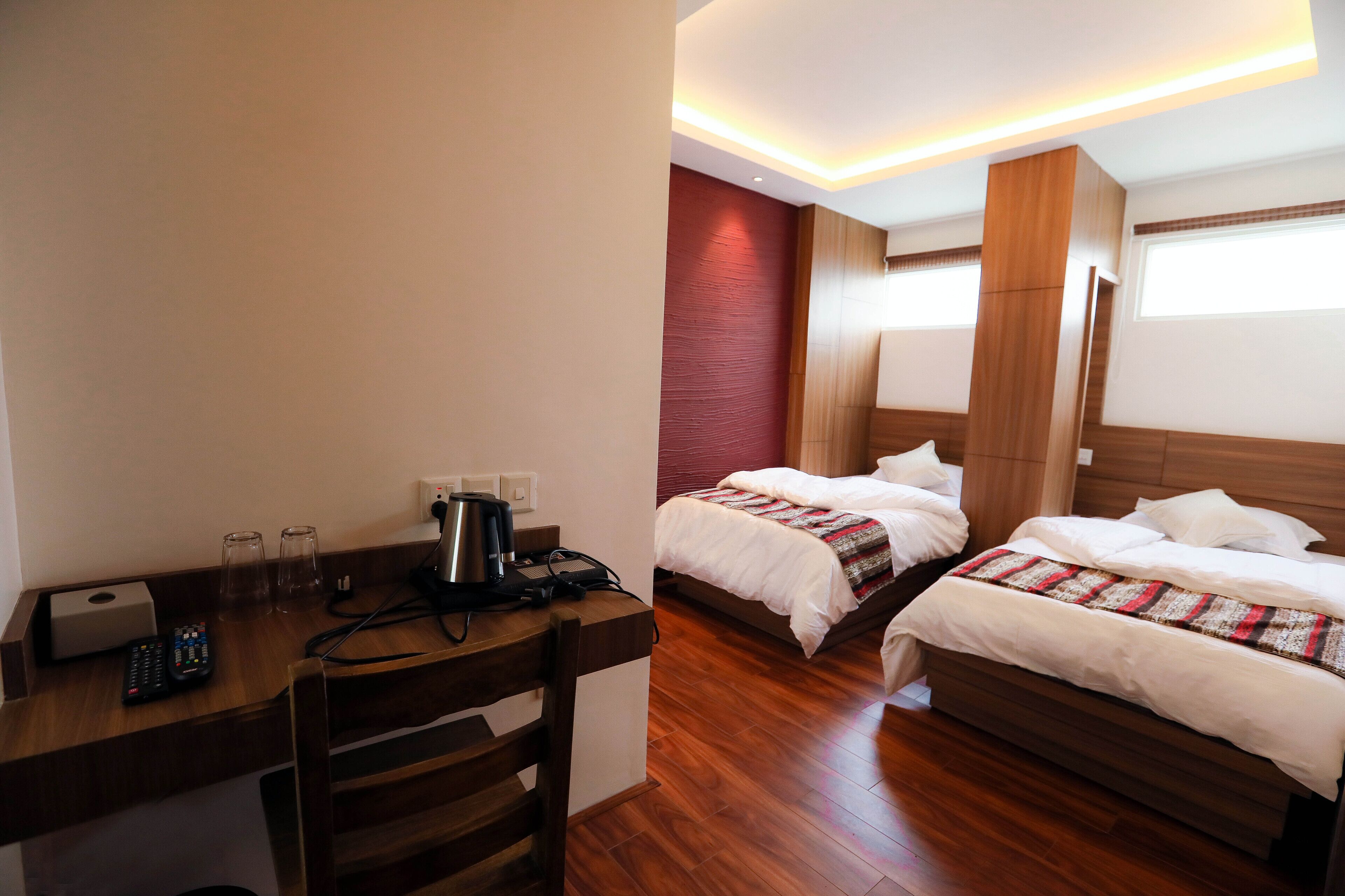 Ein Hotelzimmer mit einem hölzernen Schreibtisch, zwei Betten, einer roten Akzentwand und einem Fenster mit Jalousien.