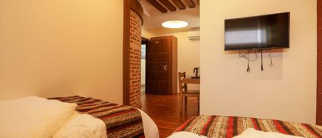 Habitación de hotel con dos camas, un televisor montado en la pared y techo de madera.