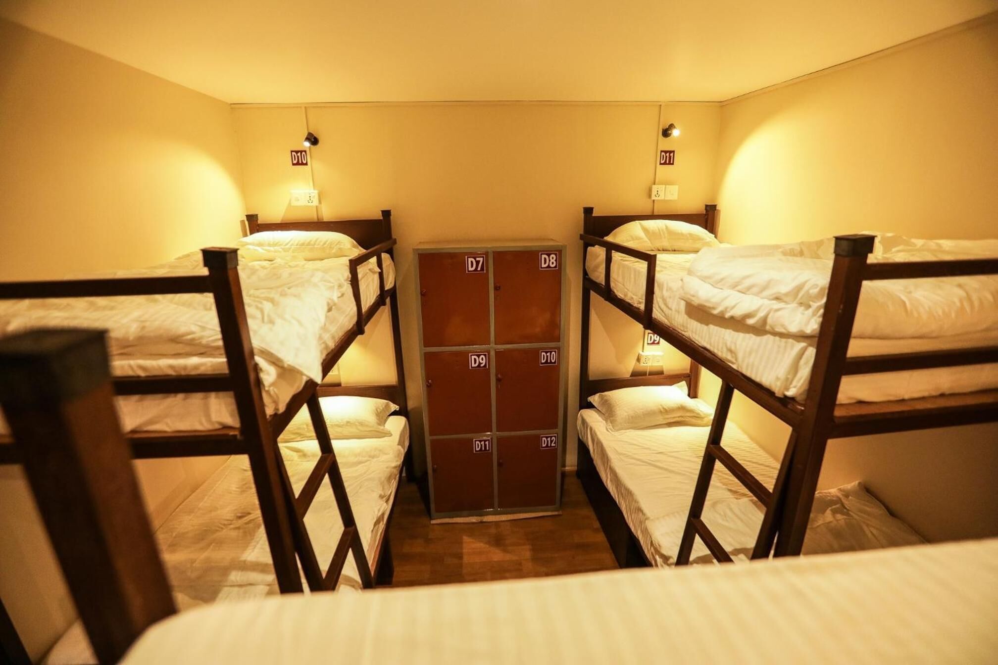 A dormitory room with bunk beds, a wardrobe with multiple compartments, and wall-mounted lights.