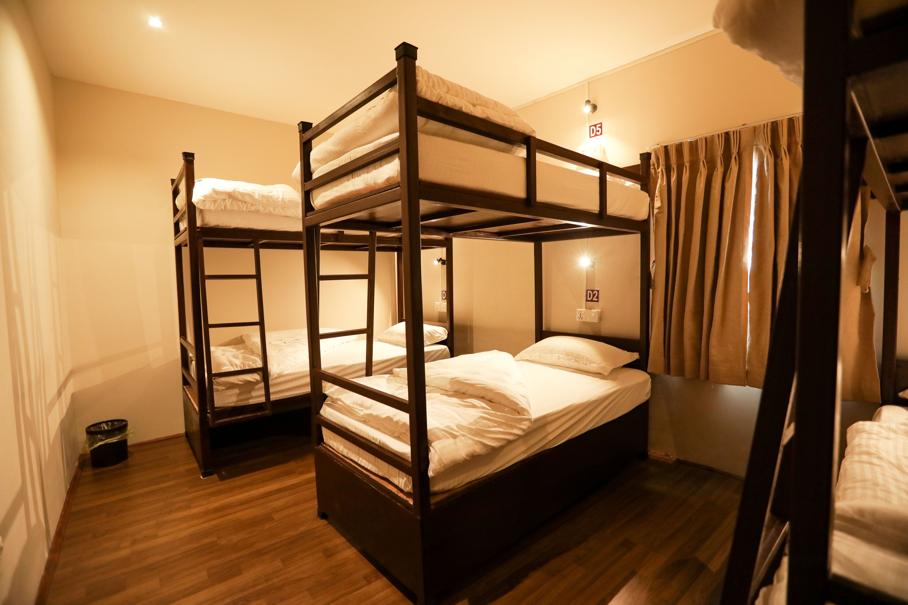 A room with three bunk beds, wooden flooring, and a curtain on the window.