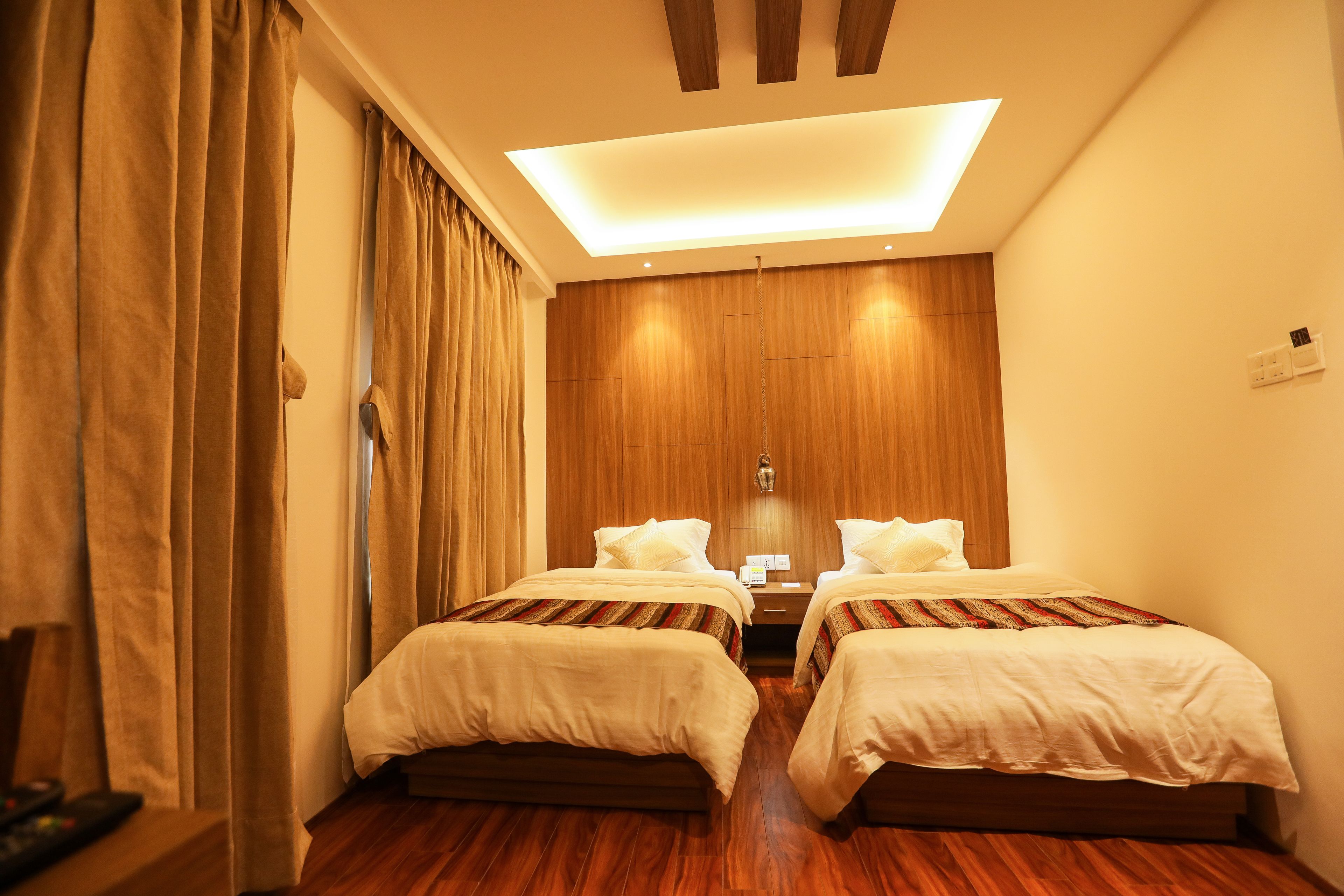 A hotel room with two beds, wooden flooring, a ceiling light, and a wooden wall panel.