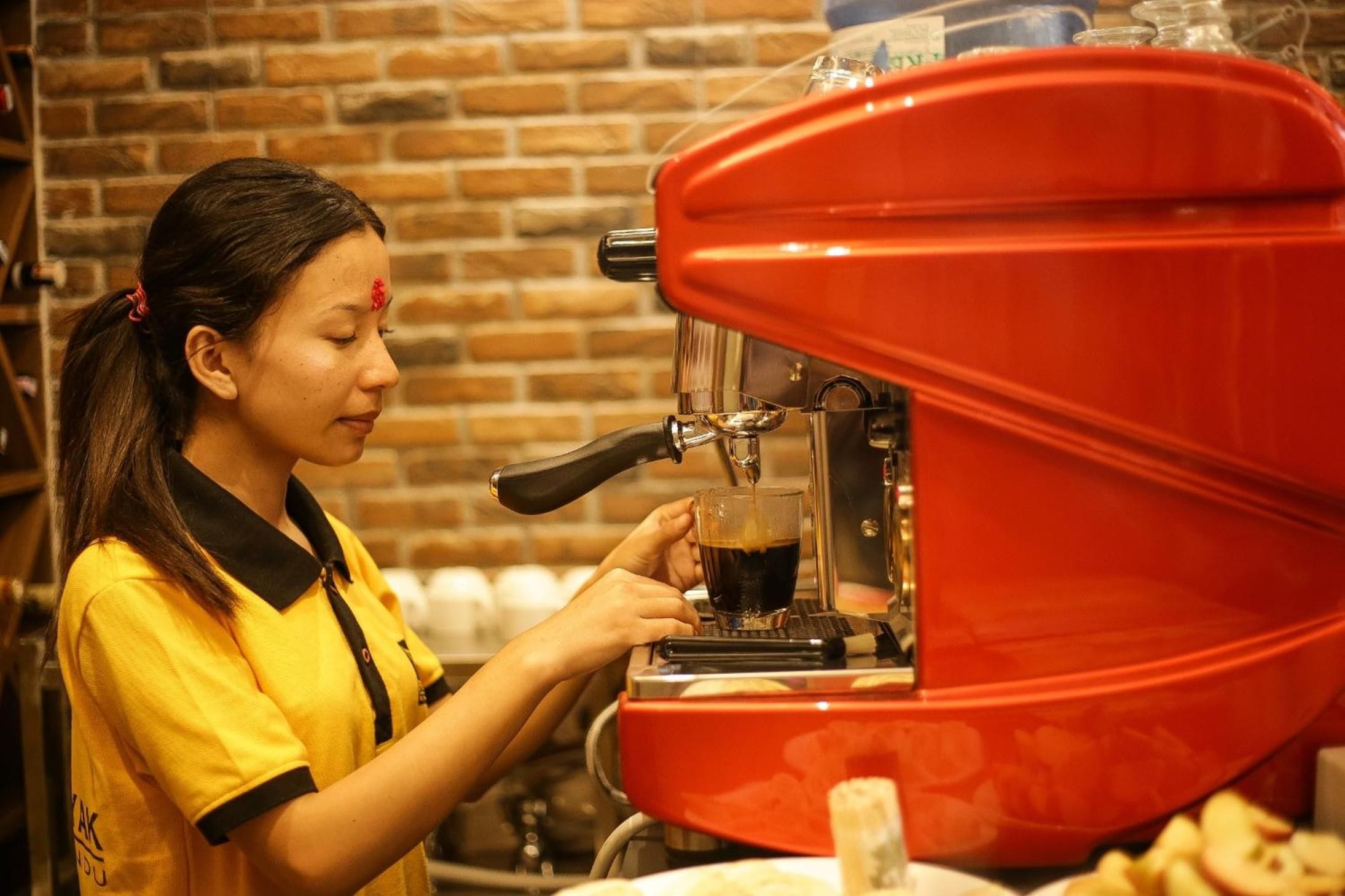 A person operating a red coffee machine, likely in a cafe or restaurant setting.