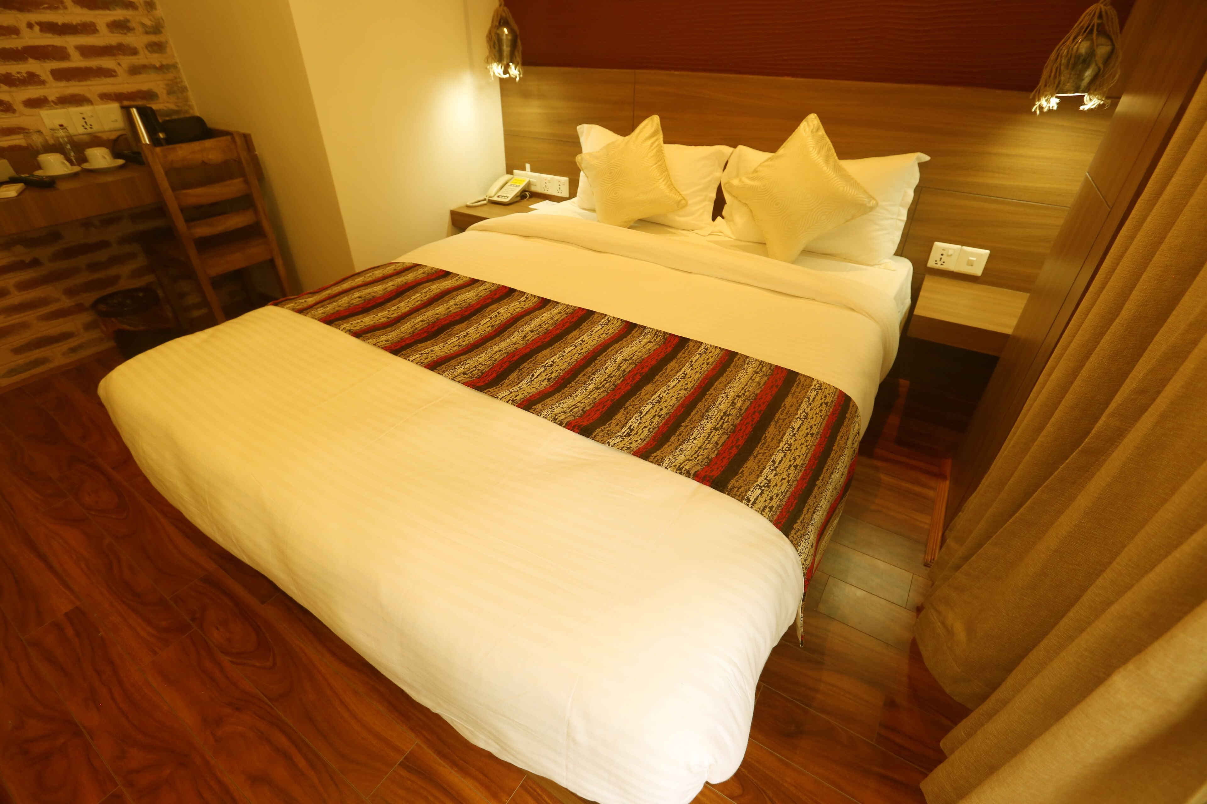 Una cama bien hecha con una colcha a rayas, un cabecero de madera y una mesita de noche con una lámpara y un teléfono.