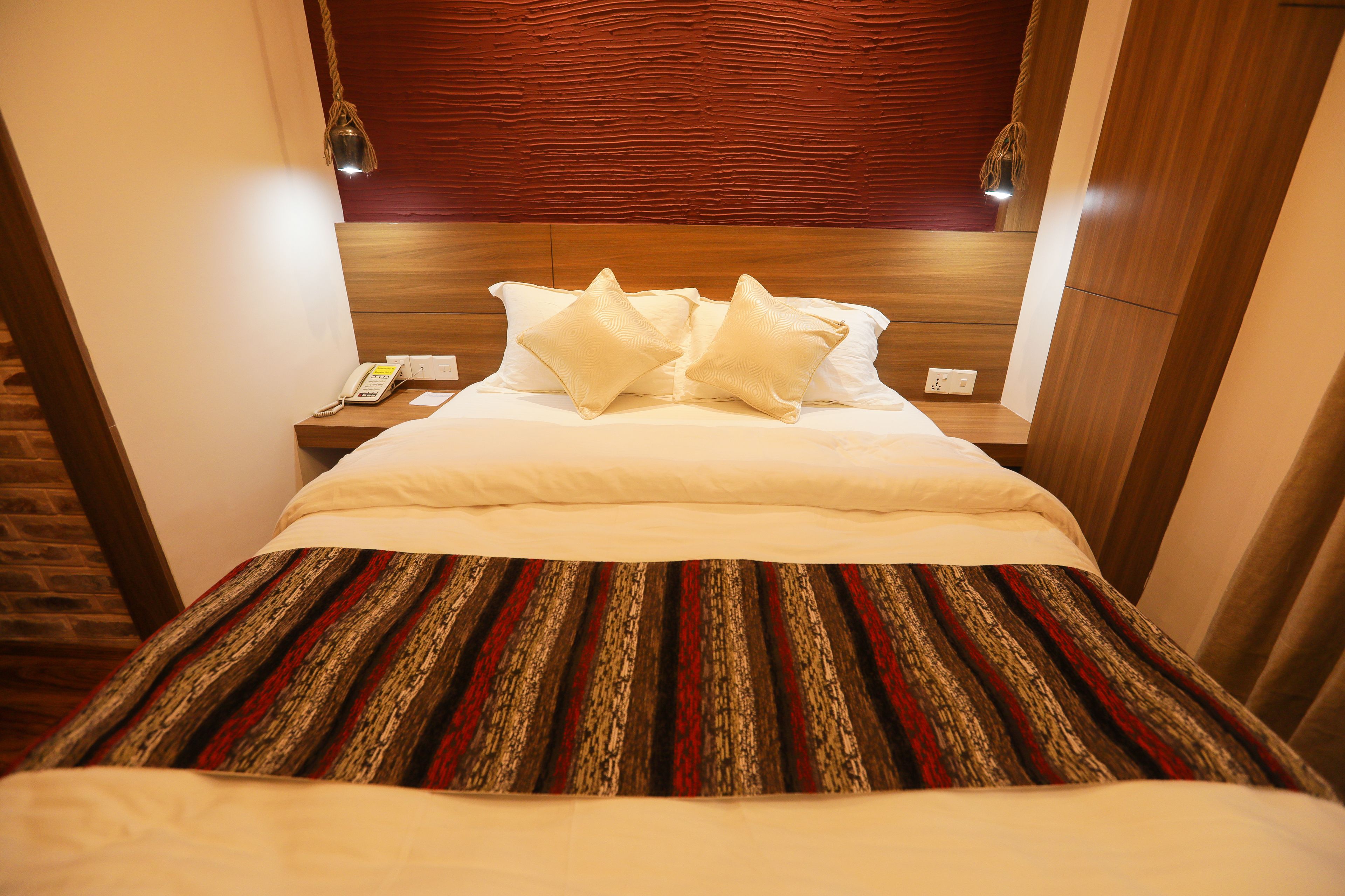 Une chambre d’hôtel avec une tête de lit en bois, une couvre-lit à rayures et deux oreillers blancs.