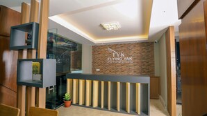 A reception desk with a modern design, a brick wall with the logo "Flying Yak Kathmandu", and a potted plant. - Flying Yak Hotel - Hostel (Kathmandu)