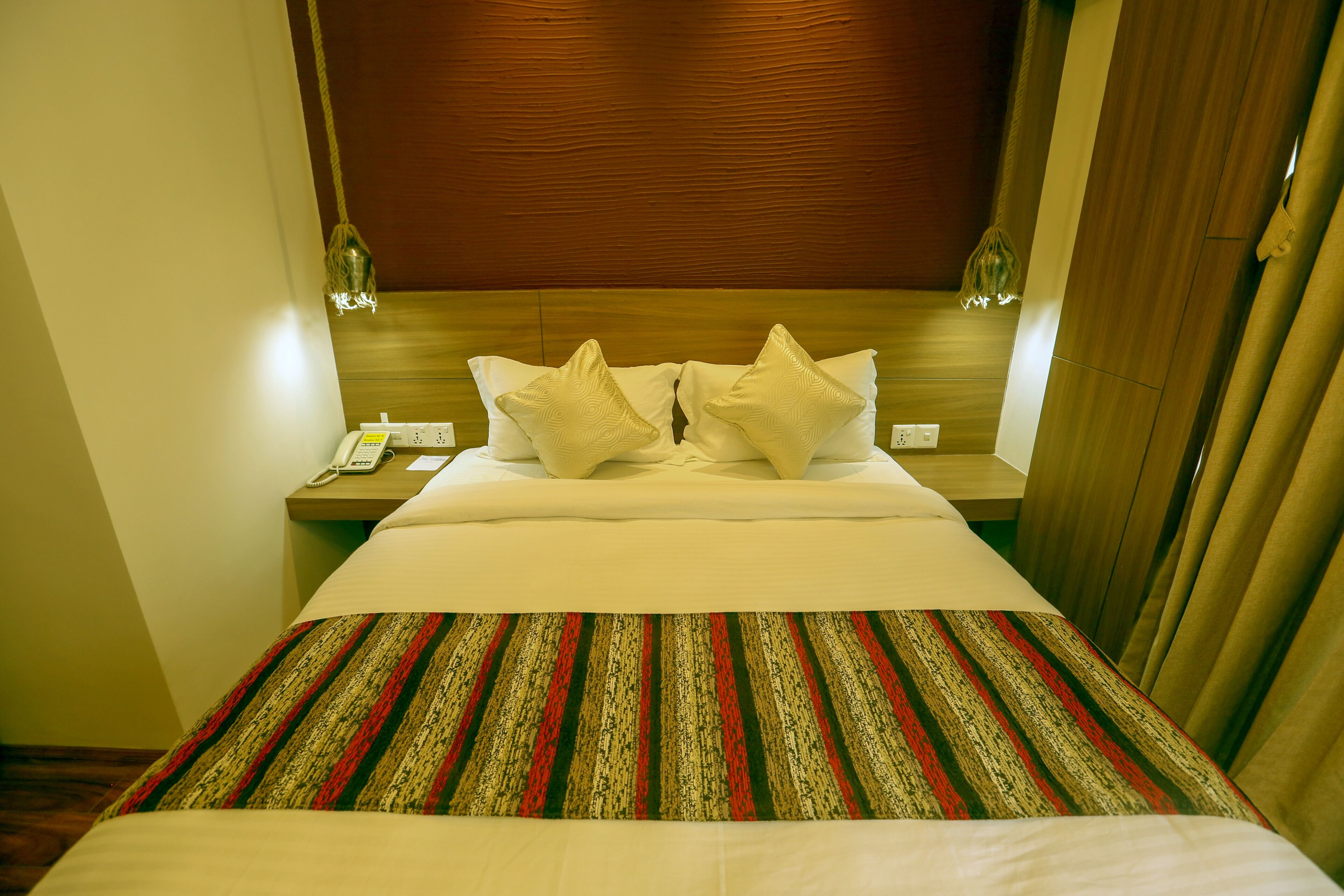 Una habitación de hotel con cabecera de madera, colcha a rayas y dos almohadas.