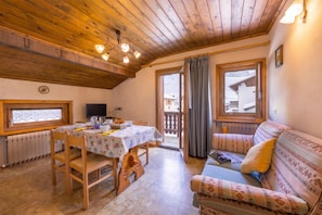 A cozy room with a wooden ceiling, a dining table with chairs, a sofa, and a window with a view of a snowy landscape. - Eden Ski in - Ski out 50m, Livigno, Italy (Livigno)