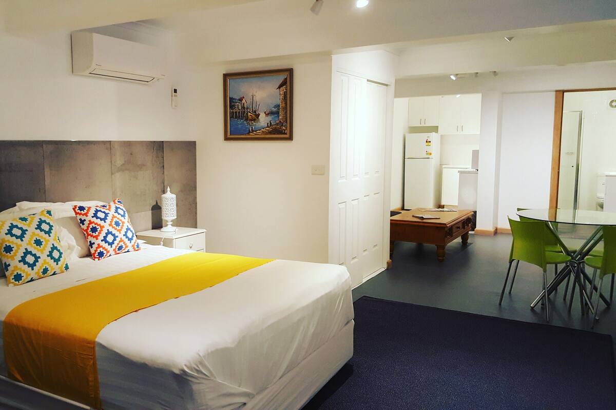 A hotel room with a bed, bedside table, lamp, and a painting on the wall.