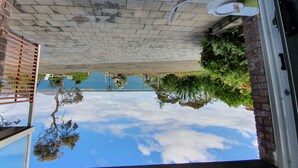 Udsigt gennem et vindue med klar himmel, en murstensvæg og refleksioner af træer og et bassin.